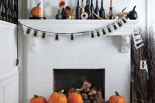 a refined Halloween mantel with black and orange candles, a bug garland a top hat, various pumpkins and black bottles