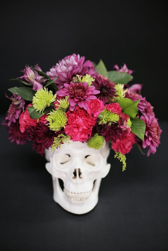 a skull with a bold floral arrangement in pink, red and green plus some leaves is a timeless idea for Halloween