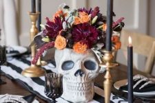 a skull with dark blooms and black candles in brass candleholders for a chic Halloween tablescape