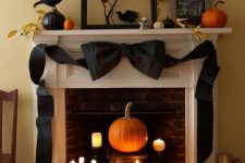 a sophisticated Halloween mantel with pumpkins, blackbirds, branches with leaves, a giant black bow and candles in the fireplace