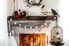 a stylish Halloween mantel with black spiderweb, lots of candles, skulls and black and gilded pumpkins plus blackbirds