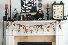 a vintage Halloween mantel with a bunting, blackbirds, orange candles, bars and vintage books and clocks