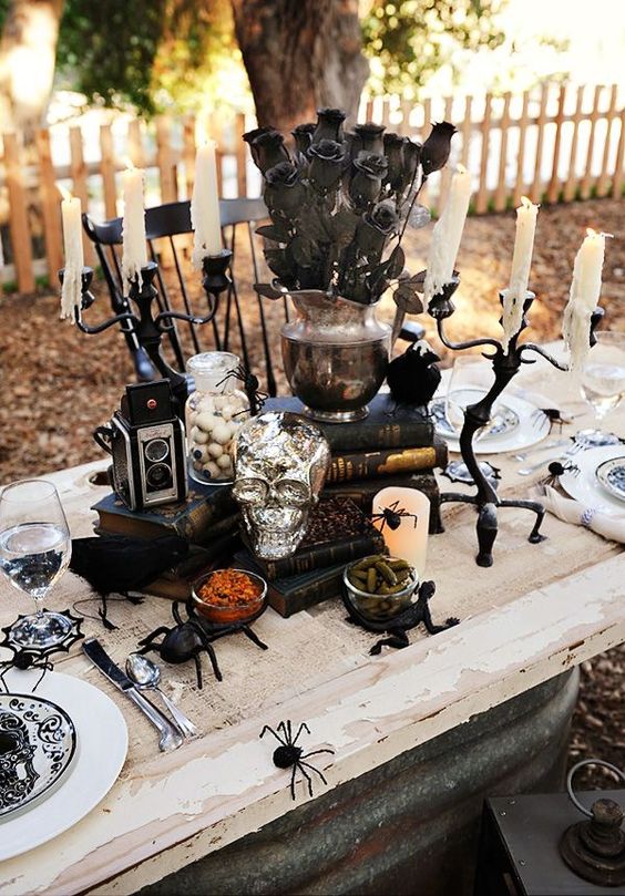 a whimsical Halloween centerpiece of black books, black roses in a vase, eyeballs, a skull, a vintage camera and spiders
