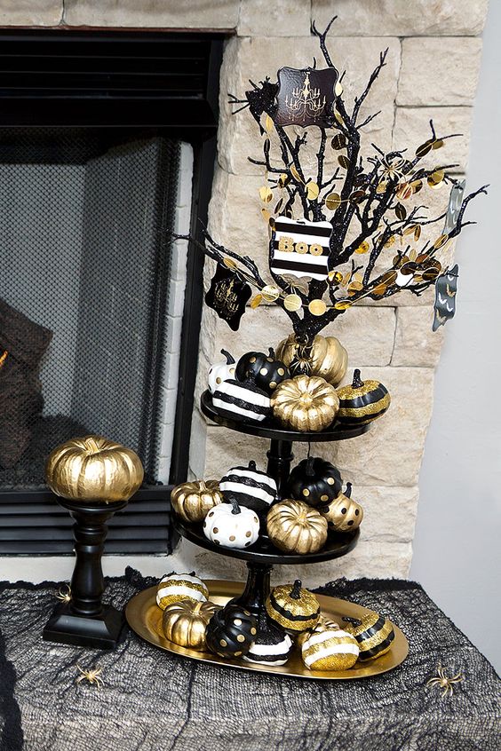 a black Halloween tree with gold garlands, with a stand with black, white and gold pumpkins under it