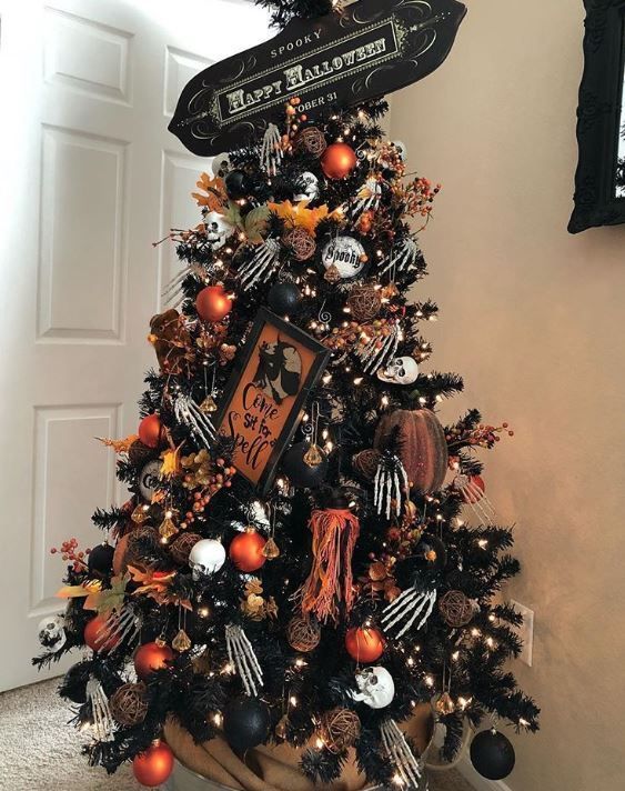 a black Halloween tree with white, black and orange ornaments, skeleton hands, skulls and a sign on top