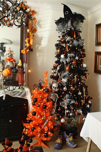 a black lit up Halloween tree, with skeletons, spiders, bright ornaments and a mini orange tree with black ornaments