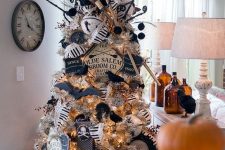 a white Halloween tree with lights, black ornaments, black and white garlands, twigs and a witch hat on top