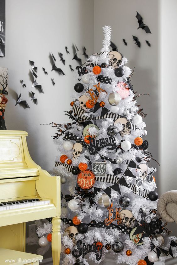 a white Halloween tree with white, grey, silver, orange and black ornaments, garlands and skulls