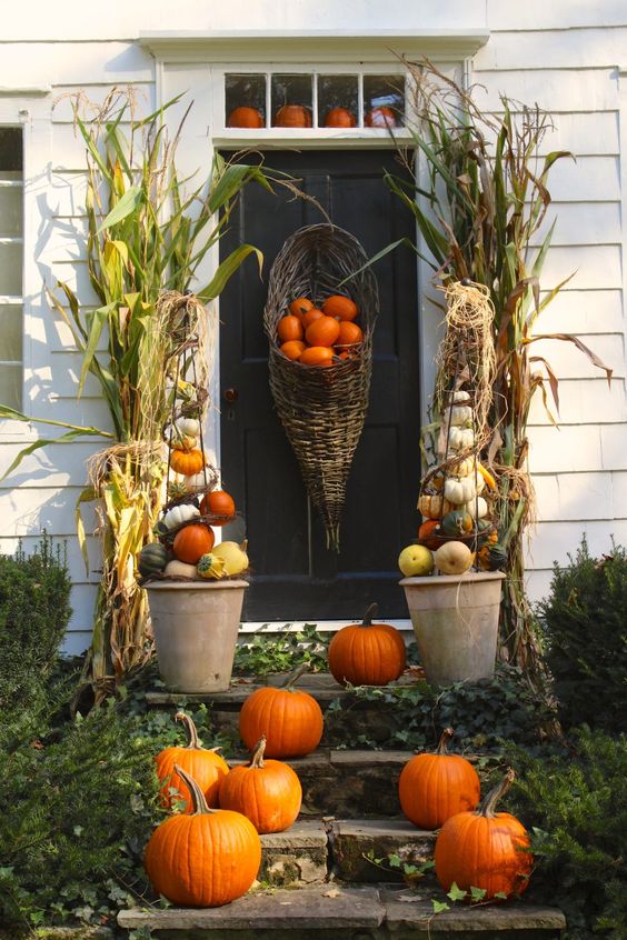a Thanksgiving porch with orange, white and green pumpkins in cones and on the steps, corn husks and a cornucopia with pumpkins