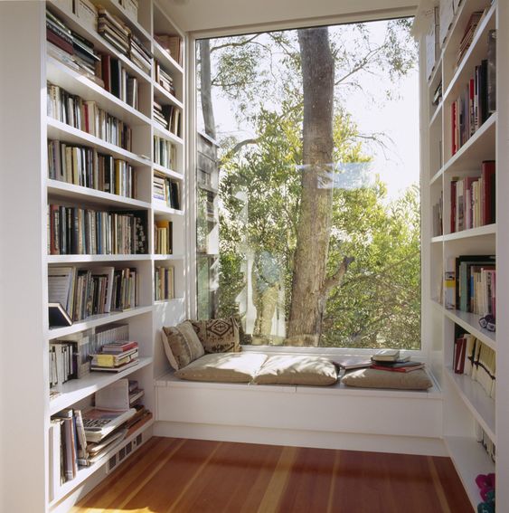 a contemporary windowsill nook with a bench with pillows and cushions and lots of bookshelves taking each wall