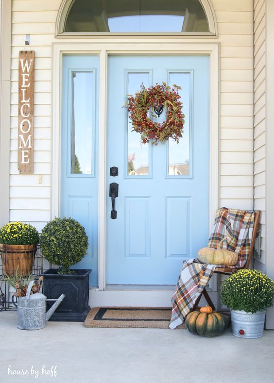 a cool Thanksgiving porch with a fall wreath, potted blooms and greenery and natural pumpkins is lovely