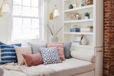 a cool windowsill reading nook with bright pillows, wall sconces and built-in shelves and neutral shades