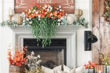 a cozy Thanksgiving mantel with lush greenery and blooms, faux pumpkins, an oversized sign and cotton and leaves in a basket