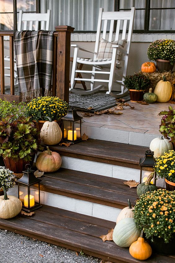 a cozy Thanksgiving porch with fall leaves, candle lanterns, pumpkins and gourds and bright potted blooms