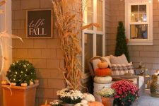 a cozy Thanksgiving porch with lots of pumpkins stacked, candles, corn husks and potted blooms