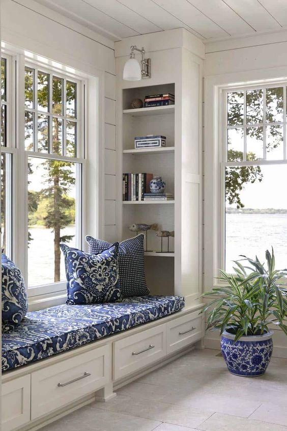 a cozy windowsill reading space with an upholostered windowsill bench with storage, built in bookshelves and sconces