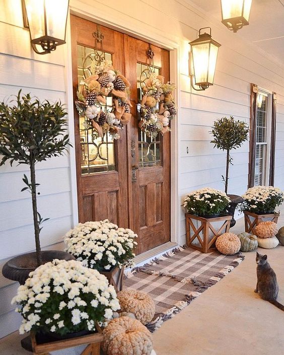 a farmhouse Thanksgiving porch with white potted blooms, heirloom pumpkins, wreaths of burlap and pinecones