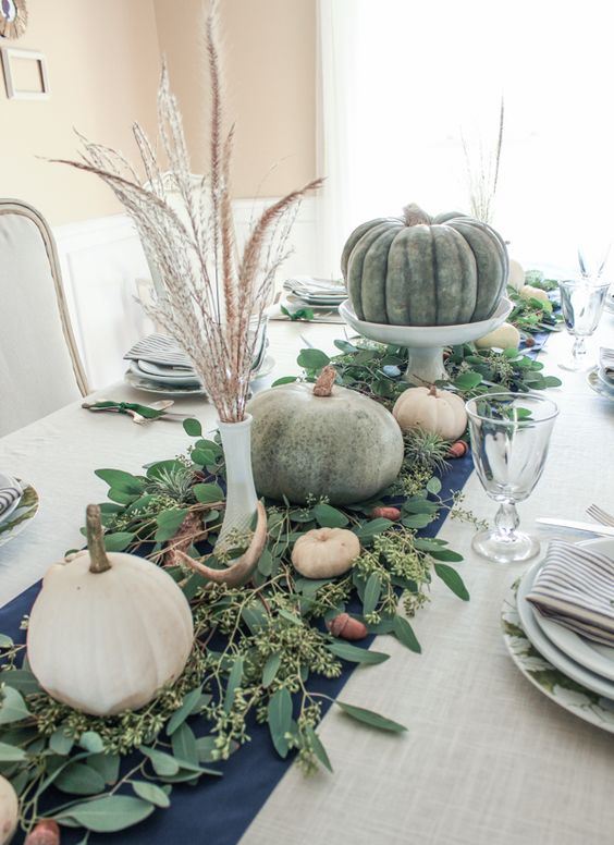 a harvest Thanskgiving centerpiece of fresh eucalyptus, antlers, white and green pumpkins and wheat in vases