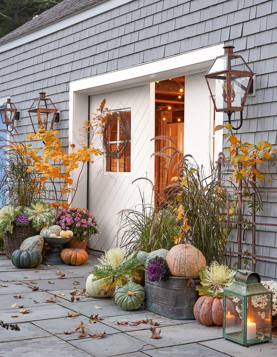 a harvest porch with usual and heirloom pumpkins, candle lanterns, bold leafy branches and grass is veyr natural