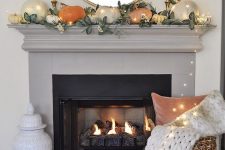 a modern Thanksgiving mantel with large pumpkinsm leaves, candles and lights is a very chic idea