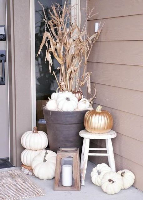 a neutral Thanksgiving porch with white pumpkins, a candle lantern, corn husks and gold pumpkins is elegant