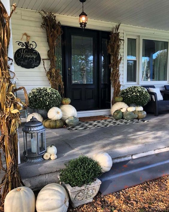a neutral fall porch with white and green pumpkins and gourds, a printed rug, white blooms in pots