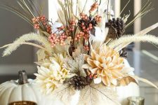 a rustic Thanksgiving centerpiece of a white pumpkin, dried leaves, blooms, berries, grasses and pinecones