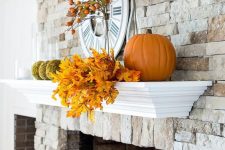 a rustic mantel with fall leaves, moss balls, pumpkins and fruits on the branches is suitable for both fall and Thanksgiving
