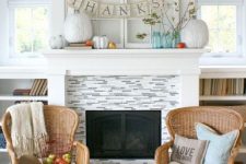 a simple Thanksgiving mantel with white and colorful pumpkins, branches with leaves and banners is a cool idea