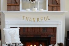 a stylish Thanksgiving mantel with white pumpkins, a cotton wreath and candles on a stand in the fireplace