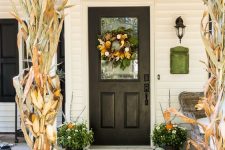 a stylish fall porch with corn husks, green, white and orange pumpkins, candle lanterns and a fresh fall wreath