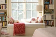 a traditional windowsill reading nook with an upholstered bench, with built-in shelves and bright pillows and a blanket