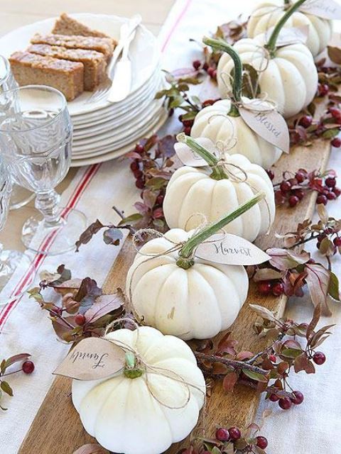 a wooden board with berries, leaves and white pumpkins with tags is a simple rustic centerpiece for the fall