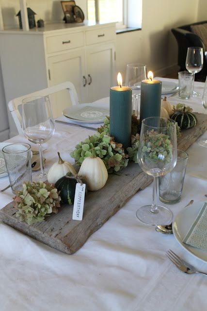 a wooden board with green hydrangeas, green candles, white pumpkins and gourds is a rustic Thanksgiving centerpiece