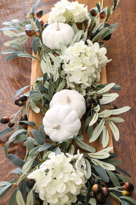 a wooden bowl with olive branches and leaves, white hydrangeas and pumpkins for Thanksgiving