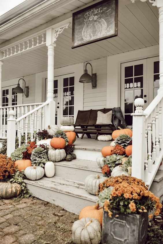 an all-natural fall porch with grey, white and orange pumpkins, bright orange potted blooms and a chalkboard sign