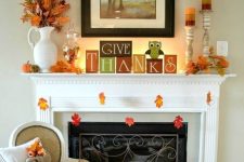 an easy and bright Thanksgiving mantel with bright cubes, colorful candles in candleholders, faux pumpkins and fall leaves