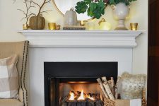 an elegant fall mantel with candles in candleholders, faux pumpkins and green leaves in a chic vase