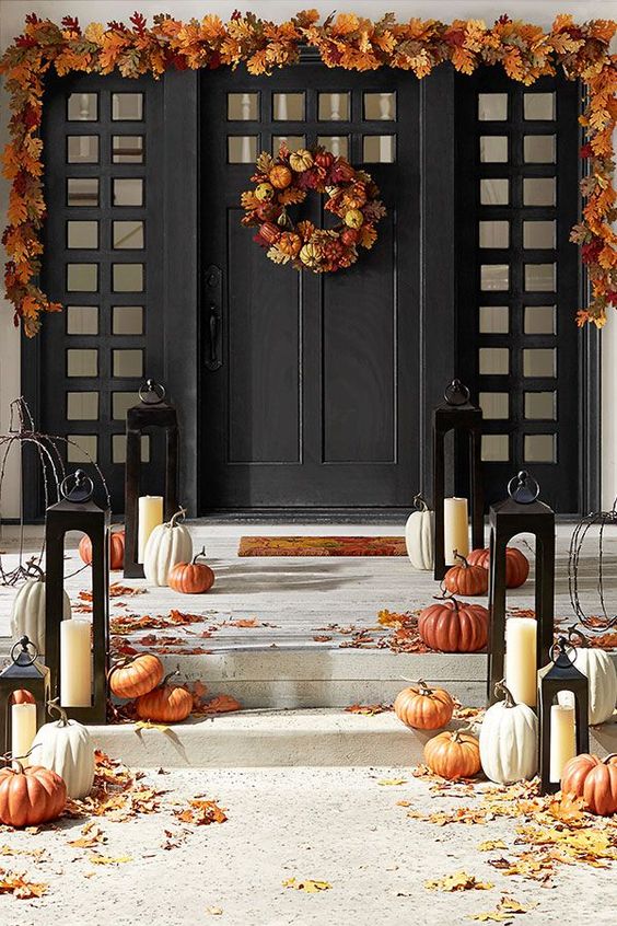 an elegant fall porch with pumpkins, leaves and candle lanterns, leaves and pumpkin wreath and a leaf garland