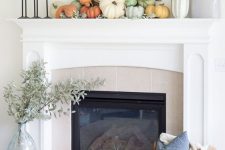 bright pumpkins and pale greenery, a wheat wreath and pale greenery in a vase next to the fireplace