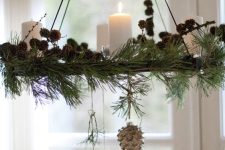 a Christmas chandelier covered with evergreens, pinecones, pillar candles and pinecone ornamnets