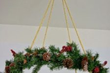 a Christmas chandelier done with evergreens, berries and pinecones is a col decoration