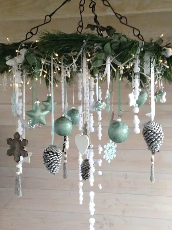 a Christmas chandelier with evergreens and greenery, lights, light green ornaments, wooden snowflakes and hearts and snowy pinecones