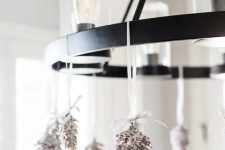 a bulb chandelier decorated with snowy pinecones is a cool and chic idea for the holidays, it’s quite rustic