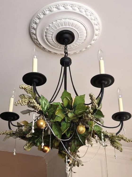 A classic candle style chandelier decorated with greenery, beads and gold glitter ornaments for the holidays