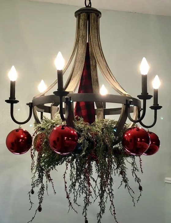 a cool vintage chandelier with greenery and red ornaments is a stylish idea for Christmas, it looks very festive