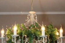 a lovely white chandelier decorated for Christmas with evergreens, beige and brown chandelier for the holidays