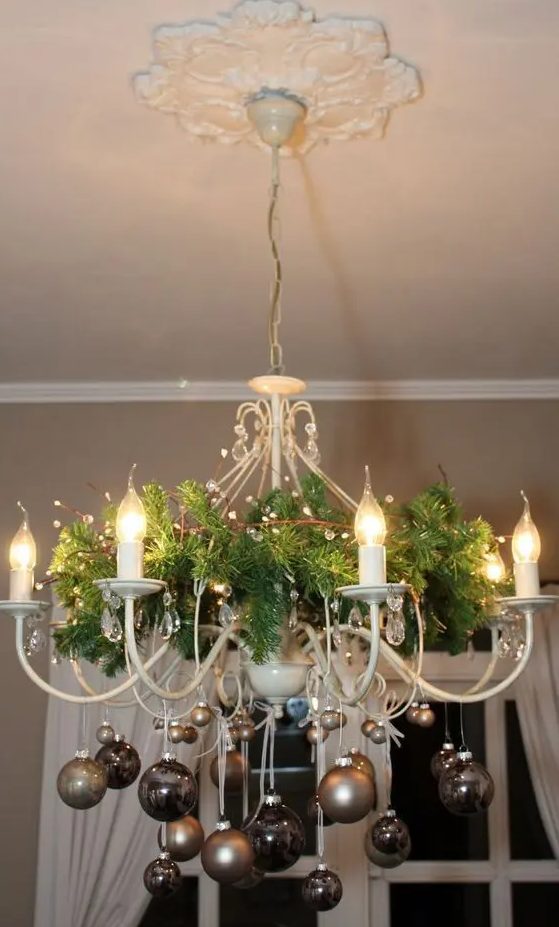 a lovely white chandelier decorated for Christmas with evergreens, beige and brown chandelier for the holidays