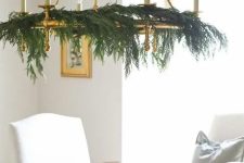 a modern gold chandelier styled with only evergreens is a stylish idea for a modern holiday space