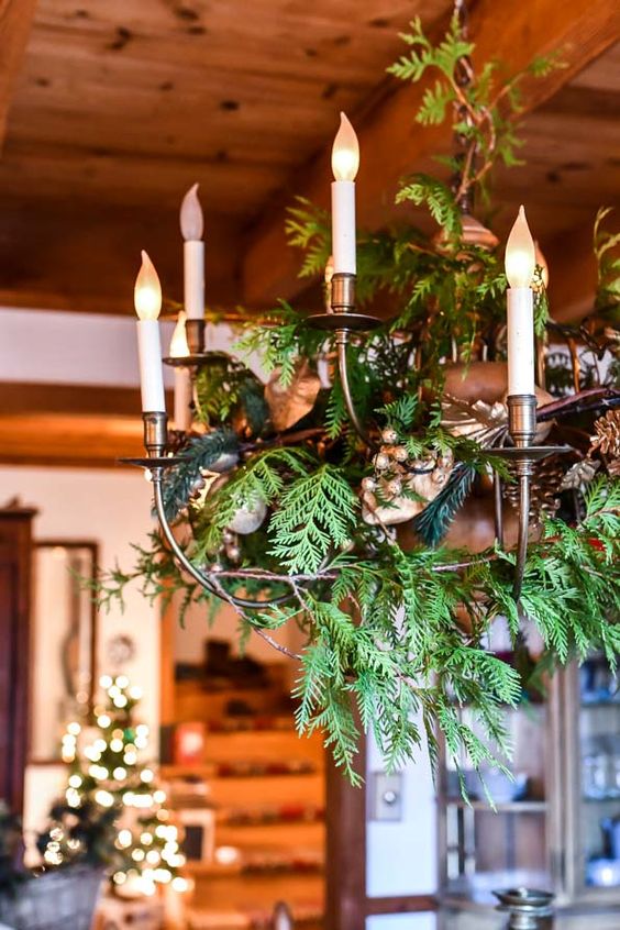 a pretty farmhouse Christmas chandelier decorated with evergreens, pinecones and leaves